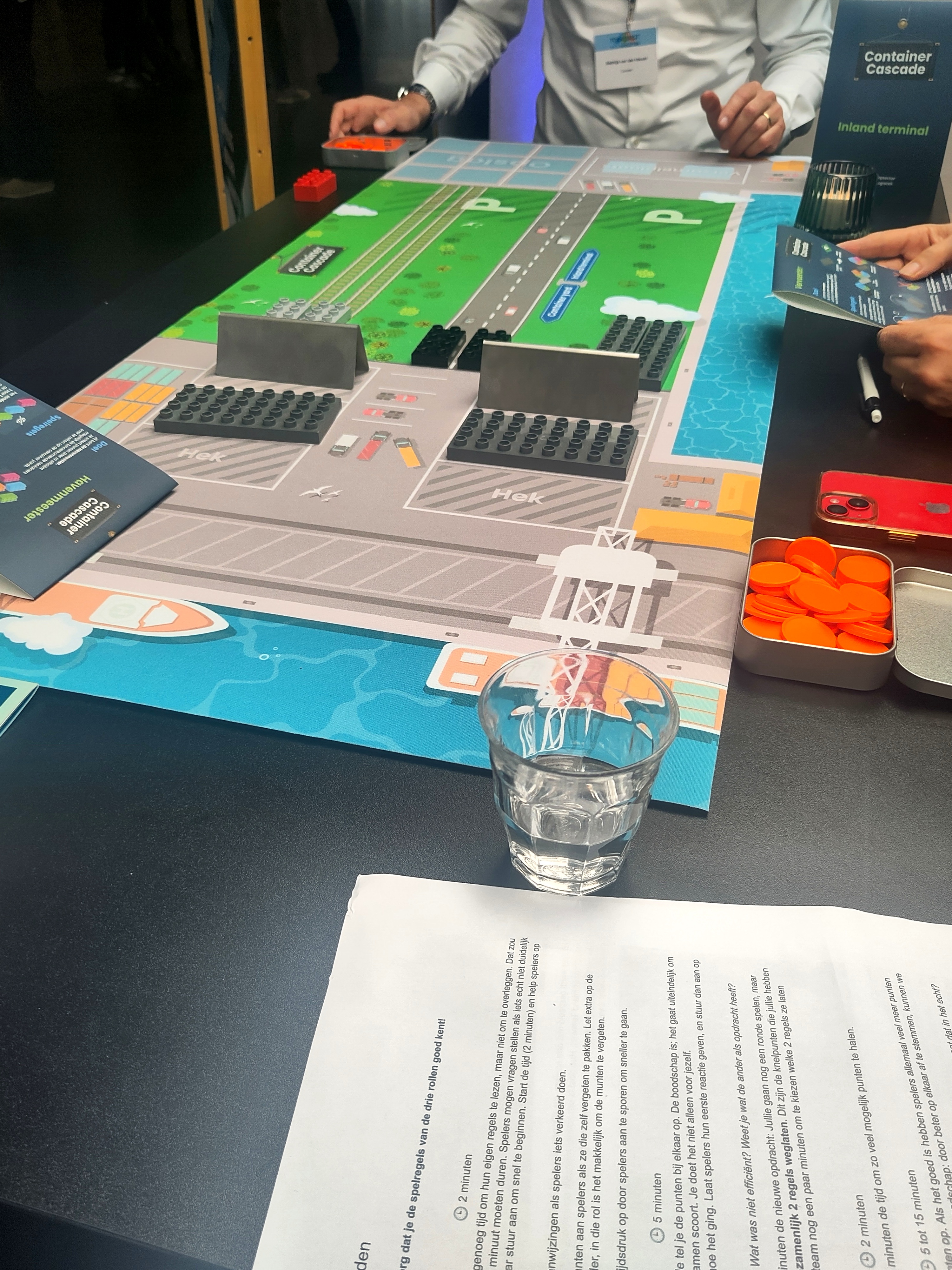 Overhead view of Container Cascade in progress, players moving containers across colorful board showing port, waterway, road and rail, orange score tokens in a tin.